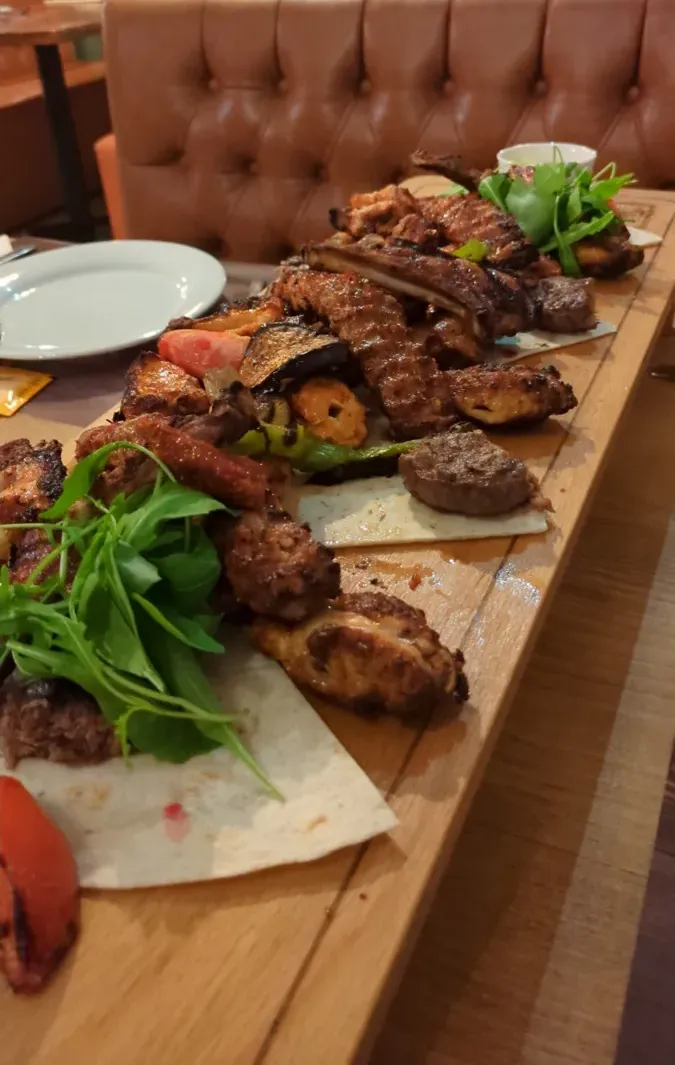 A wooden board piled with grilled kebabs, ribs, vegetables and flatbread at a Turkish restaurant