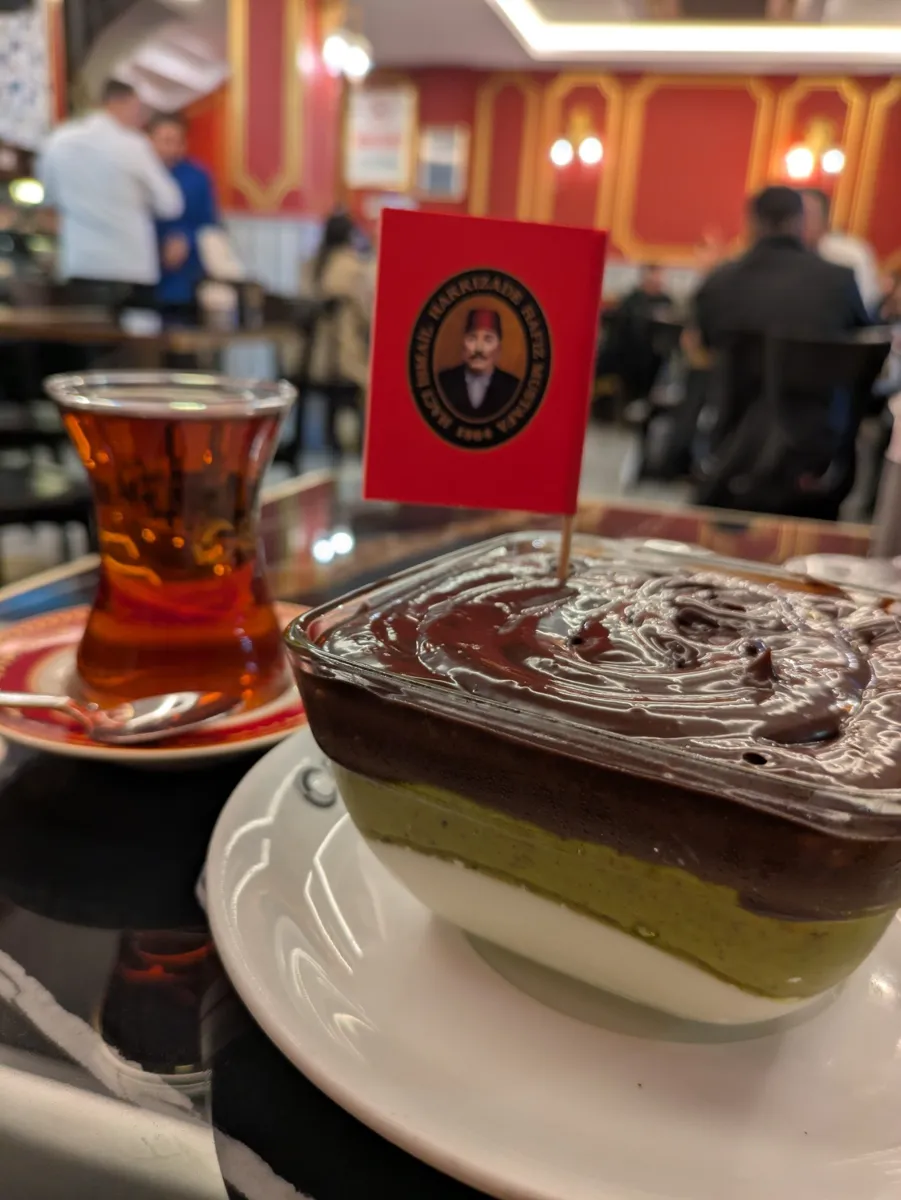 A glass of Turkish tea next to a layered chocolate and pistachio dessert at Hafız Mustafa 1864